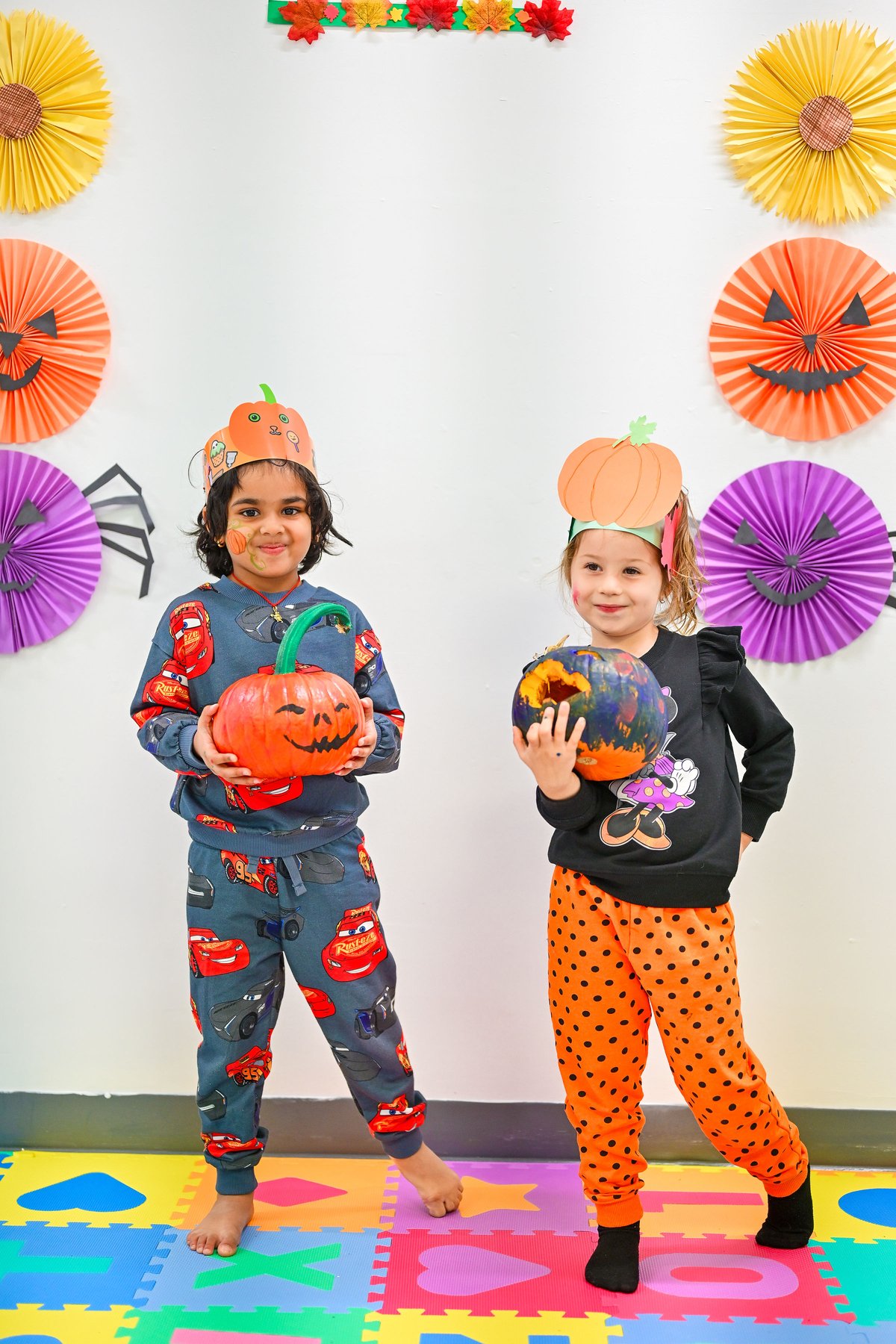 Two children in Halloween costumes with decorated pumpkins